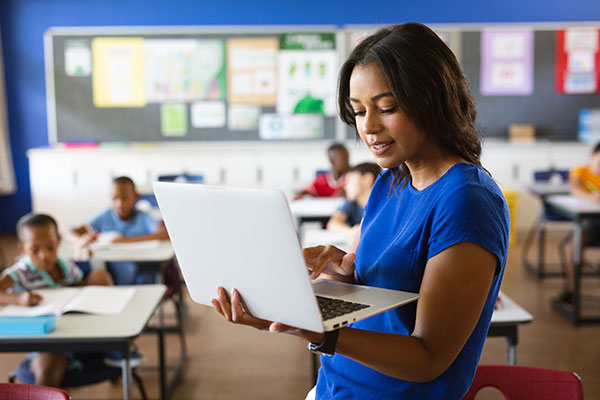 Teacher holding a laptop with her classroom in the background