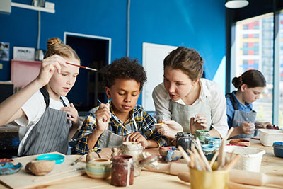 Kids wearing aprons and holding paintbrushes in an art class