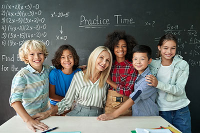 Teacher sitting with students surrounding her on each side with a chalkboard in the background